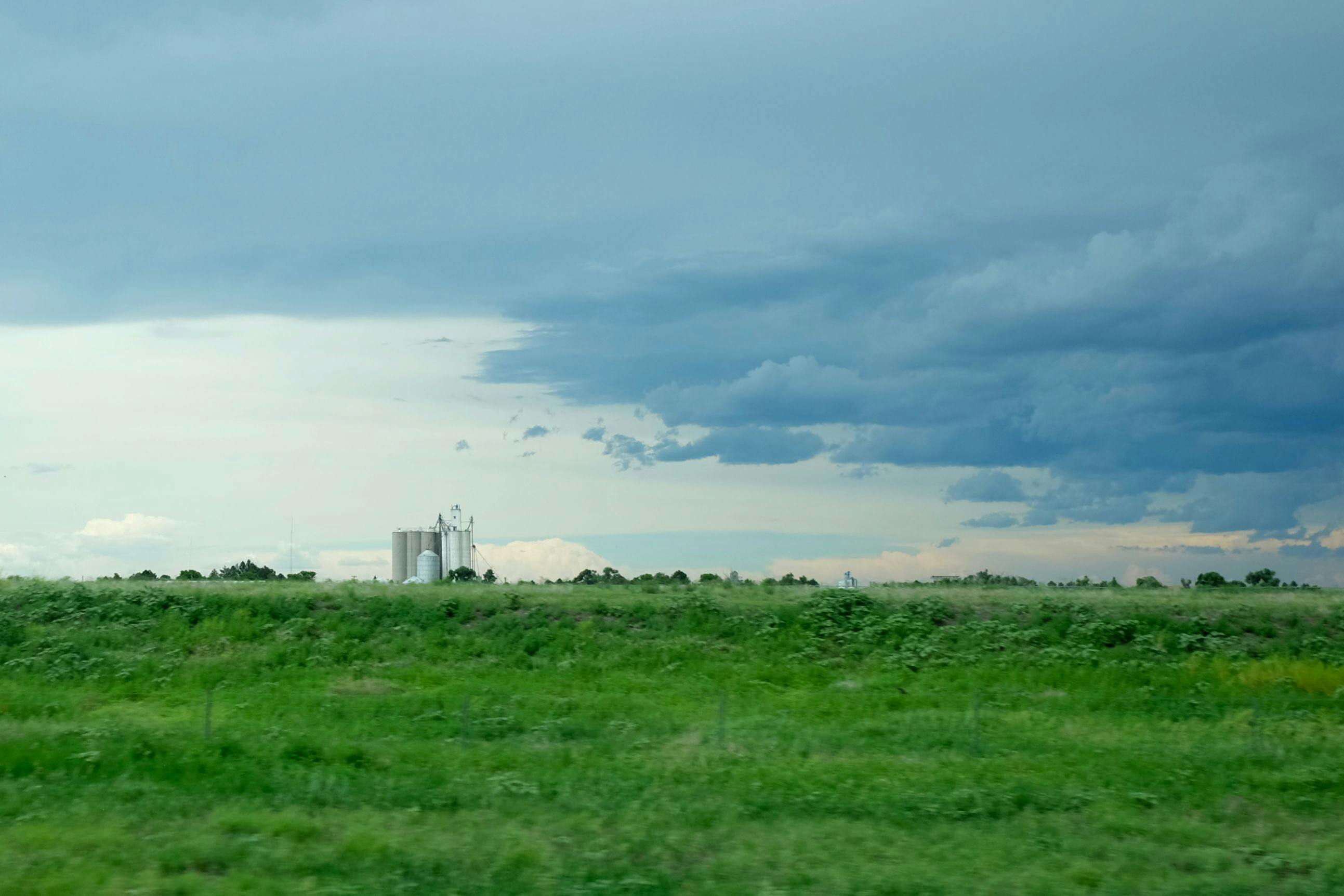 A lush green landscape with a grain silo in the distance, framed by gathering storm clouds.